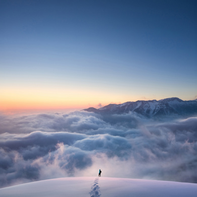 A man on top of the snowy mountain with clouds in the background.